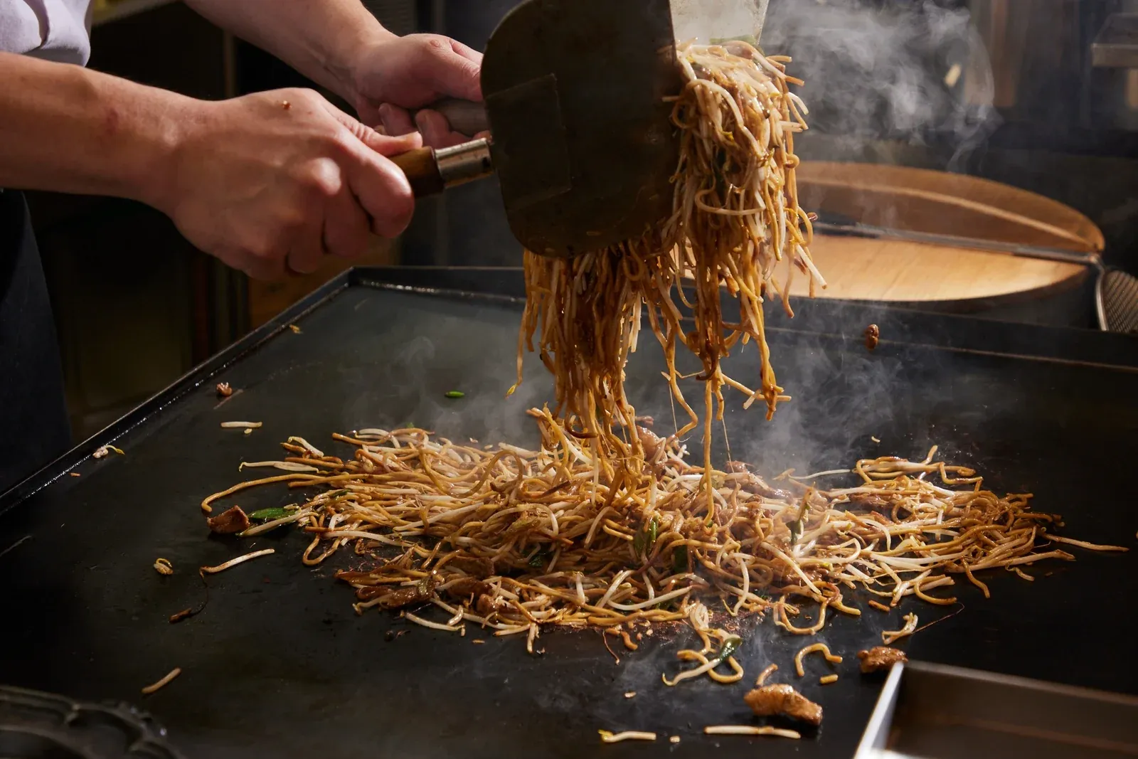 二枚のへらで麺を持ち上げ、鉄板で焼き上げる様子
